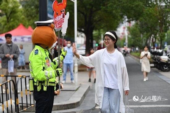 6月7日上午9時，隨著鈴聲的響起，2023年江西高考正式開考，江西省的53.57萬考生以縣（區(qū)）為單位隨機(jī)安排在全省256個考點、18968個考場參加高考。圖為“小熊交警”和考生擊掌鼓勵。 人民網(wǎng)記者 時雨攝