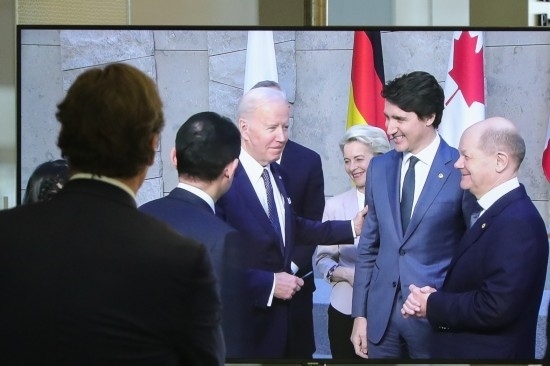 2022年3月24日，在比利時布魯塞爾的北約總部，一名男子觀看屏幕上美國總統(tǒng)拜登（右四）、歐盟委員會主席馮德萊恩（右三）、加拿大總理特魯多（右二）、德國總理朔爾茨（右一）出席七國集團峰會合影儀式的畫面。新華社記者鄭煥松攝