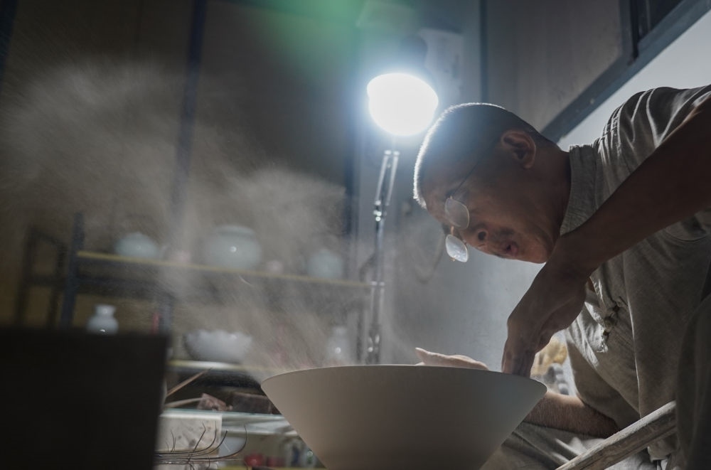 ↑ 在景德鎮(zhèn)，手工匠人吹去坯內(nèi)的泥土（2021年7月14日攝）。