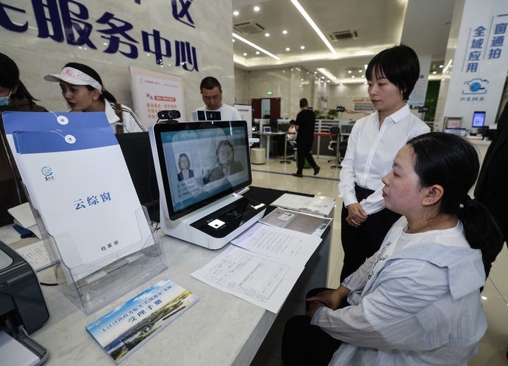 在浙江省嘉興市秀洲區(qū)王江涇鎮(zhèn)便民服務(wù)中心的“跨域通辦·云綜窗”窗口，辦理開業(yè)登記的個體工商戶（右一）通過該系統(tǒng)與江蘇省蘇州市吳江區(qū)盛澤鎮(zhèn)行政審批局工作人員視頻連線，進(jìn)行身份讀取及材料線上審核（2024年5月9日攝）。新華社記者 徐昱 攝