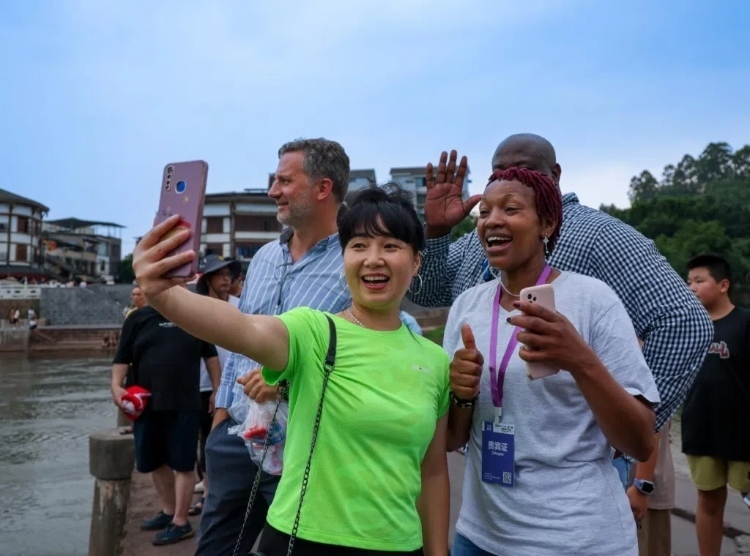 2024“一帶一路”媒體合作論壇聯(lián)合采訪調(diào)研行成員在樂山蘇稽古鎮(zhèn)與游客合影留念。本報記者 伊霄攝