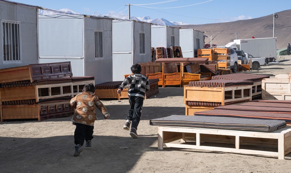 2025年1月13日，在定日縣嘎旦村，兩個孩子在剛運(yùn)來的兩排藏床間奔跑。新華社記者丁增尼達(dá) 攝